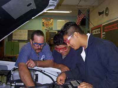 Two students and a teacher working on a car in the Auto Shop.